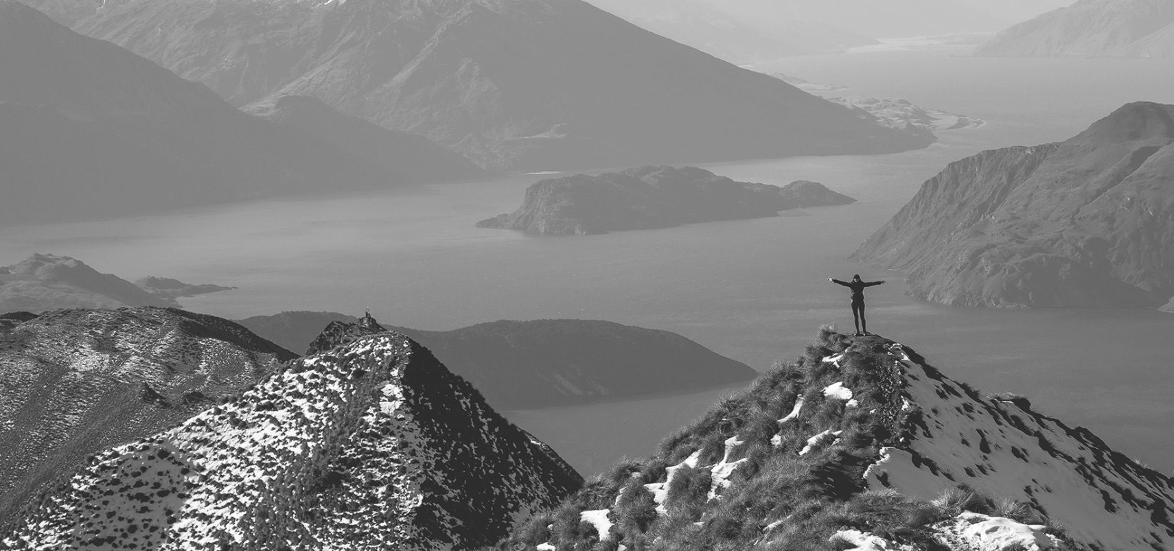 Photograph of person standing on mountain overlooking lake